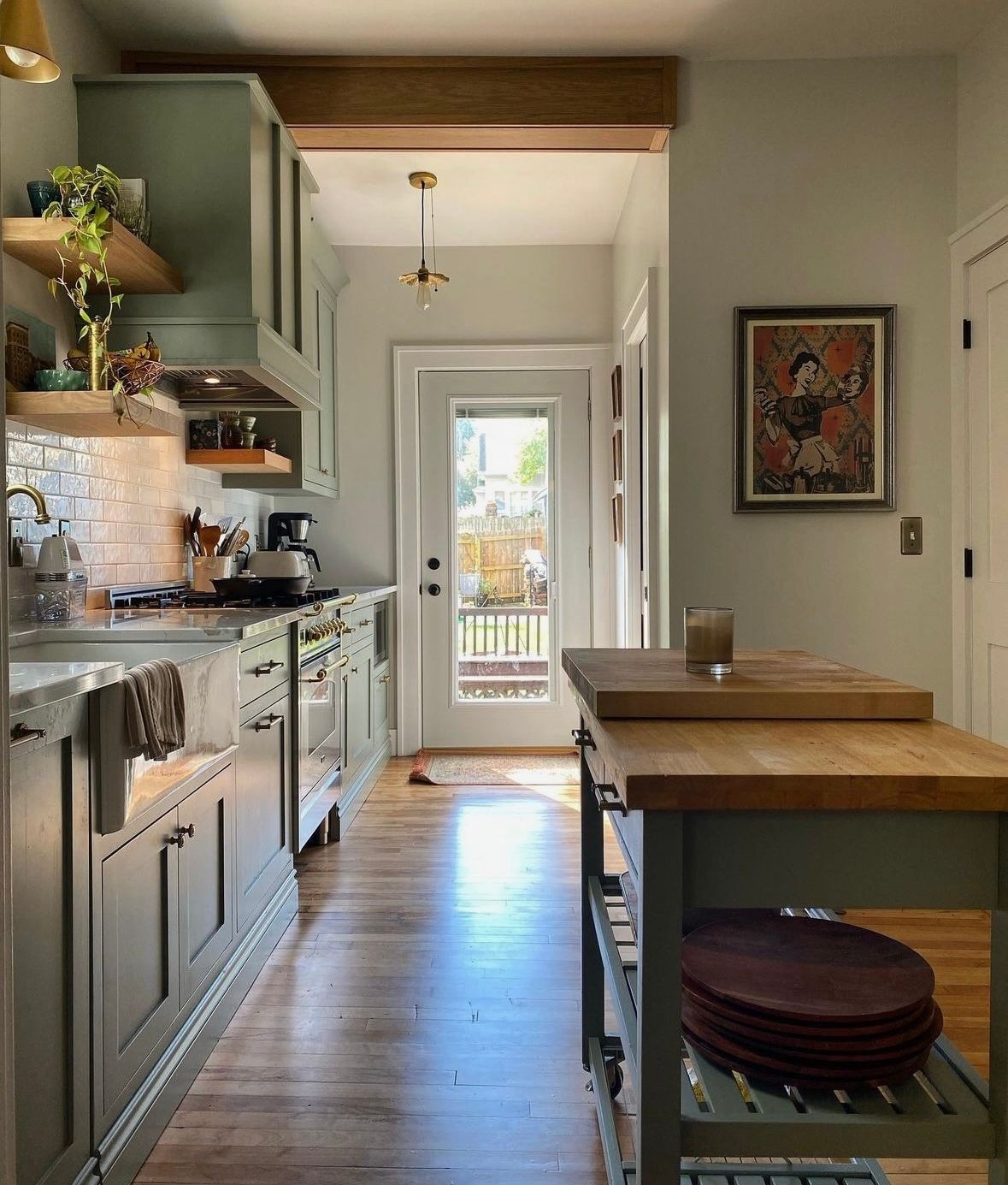 Modern kitchen with light green cabinets, a central island, and a door leading to a backyard.